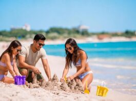 Turismo en temporada baja: viajar mejor, gastar menos y descubrir más Tres personas construyen castillos de arena en una playa de aguas turquesas, con pocos visitantes alrededor. Dos mujeres y un hombre disfrutan de una actividad recreativa junto al mar.