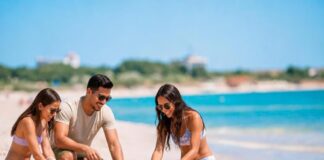 Turismo en temporada baja: viajar mejor, gastar menos y descubrir más Tres personas construyen castillos de arena en una playa de aguas turquesas, con pocos visitantes alrededor. Dos mujeres y un hombre disfrutan de una actividad recreativa junto al mar.