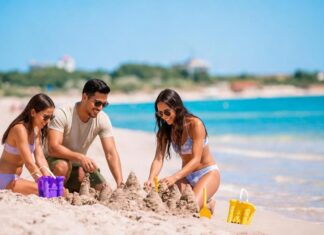Turismo en temporada baja: viajar mejor, gastar menos y descubrir más Tres personas construyen castillos de arena en una playa de aguas turquesas, con pocos visitantes alrededor. Dos mujeres y un hombre disfrutan de una actividad recreativa junto al mar.