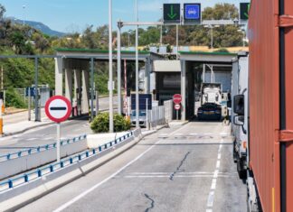 México no pagó el muro: los aranceles se cobran en Estados Unidos Camiones de carga circulan por carriles de un puesto de control con casetas, barreras y señales de tránsito.