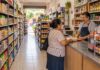 Una tiendita bien surtida también necesita proporcionar espacio para comprar Tiendita de abarrotes con anaqueles surtidos y ordenados, pasillo libre y un comerciante atendiendo a una clienta en un mostrador despejado.