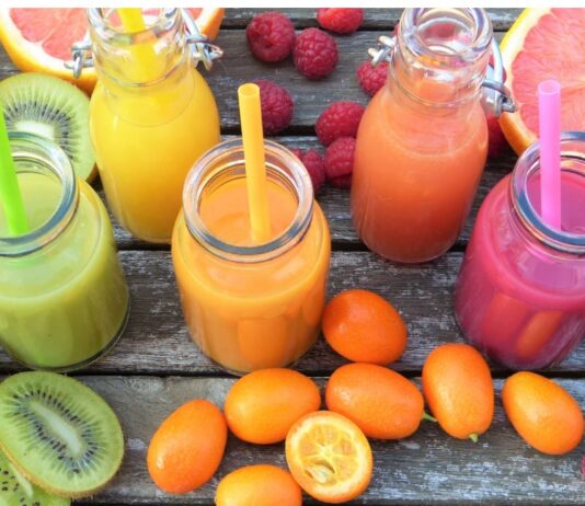 Jugos de fruta: aunque sea natural también necesita medida Vaso de jugo de naranja junto a un plato con naranja, toronja, kiwi y frambuesas sobre una mesa de madera.