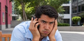 Senado aprueba multas millonarias contra las llamadas publicitarias insistentes Hombre sentado en una banca sostiene un teléfono junto al oído y se apoya la cabeza en la otra mano, con expresión de molestia.