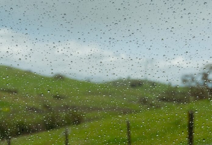 Lugar lluvioso Gotas de lluvia sobre un cristal, con un paisaje verde y un cielo gris desenfocados al fondo.