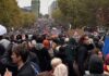 Francia vuelve a las calles pese a los toques de queda y el despliegue policial Multitud de manifestantes con pancartas y paraguas en una amplia avenida arbolada.