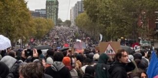 Francia vuelve a las calles pese a los toques de queda y el despliegue policial Multitud de manifestantes con pancartas y paraguas en una amplia avenida arbolada.