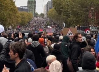 Francia vuelve a las calles pese a los toques de queda y el despliegue policial Multitud de manifestantes con pancartas y paraguas en una amplia avenida arbolada.