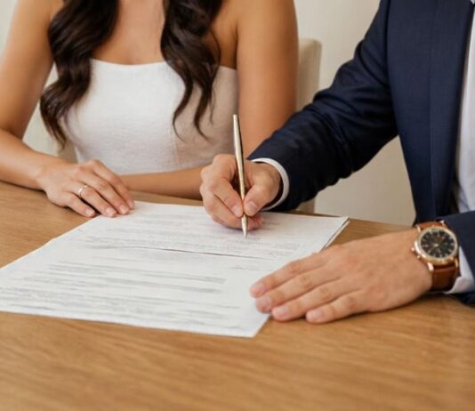 El matrimonio pierde terreno, pero conserva su fortaleza: la estabilidad Una pareja vestida de boda firma un documento sobre una mesa de madera.