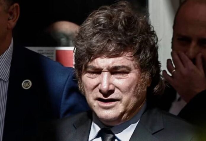 Javier Milei, con traje oscuro y corbata, rodeado de otras personas.