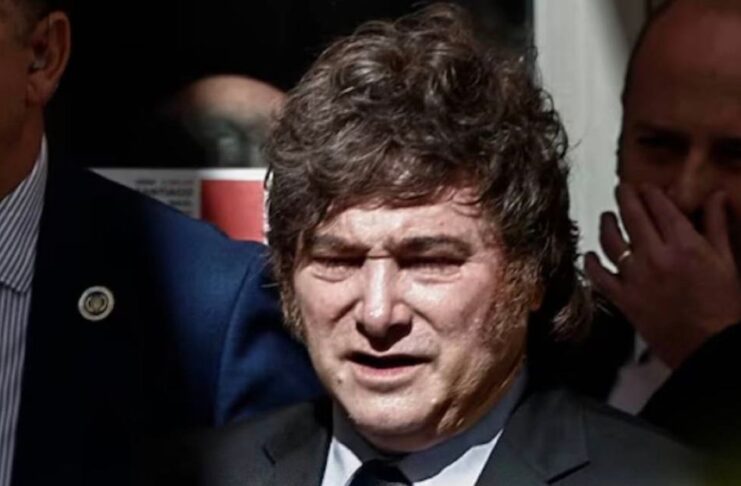 Milei en España: llama dictador, corrupto y ladrón al presidente español Javier Milei, con traje oscuro y corbata, rodeado de otras personas.