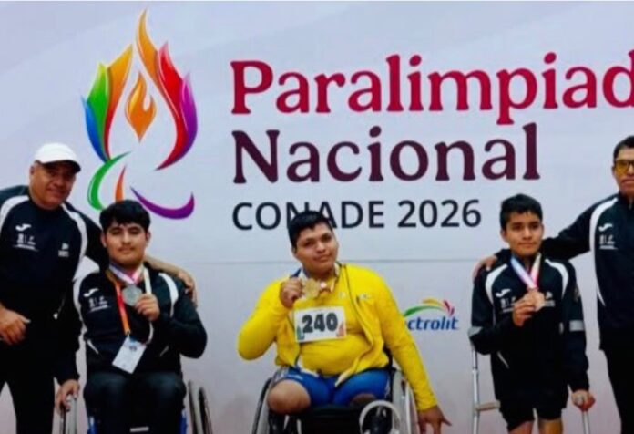 Tres deportistas con medallas, dos de ellos en silla de ruedas, posan junto a dos acompañantes frente al cartel de la Paralimpiada Nacional CONADE 2026.