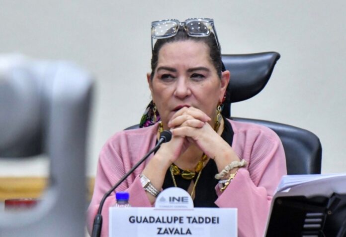 Guadalupe Taddei sentada frente a un micrófono, con las manos entrelazadas y un letrero con su nombre.