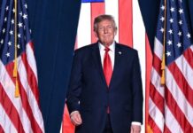 Donald Trump descalifica a Noruega por no otorgarle el premio Nobel de la Paz Donald Trump, con traje oscuro y corbata roja, frente a varias banderas de Estados Unidos.