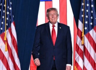 Donald Trump descalifica a Noruega por no otorgarle el premio Nobel de la Paz Donald Trump, con traje oscuro y corbata roja, frente a varias banderas de Estados Unidos.